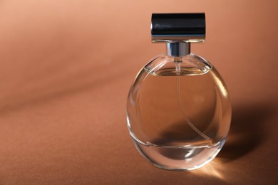 Photo of Bottle of fragrant perfume on brown background, closeup. Space for text