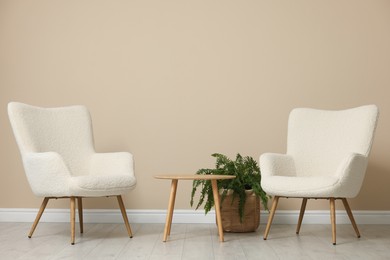 Photo of Soft armchairs and coffee table near beige wall indoors