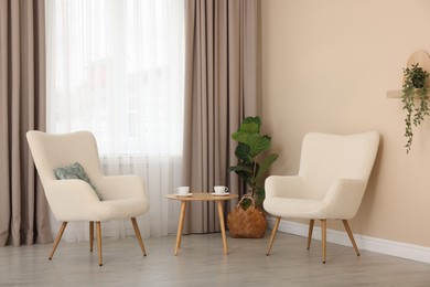 Photo of Soft armchairs and coffee table near beige wall indoors