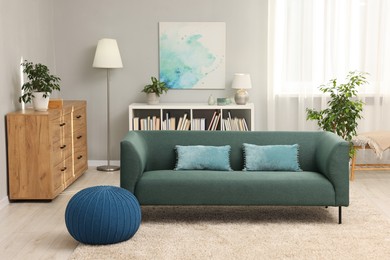 Photo of Stylish living room interior with soft sofa, pouf, houseplants and chest of drawers near grey wall