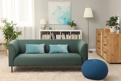 Photo of Stylish living room interior with soft sofa, pouf, houseplants and chest of drawers near grey wall