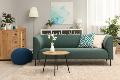 Photo of Soft sofa, coffee table, pouf, houseplants and chest of drawers near grey wall in living room. Interior design