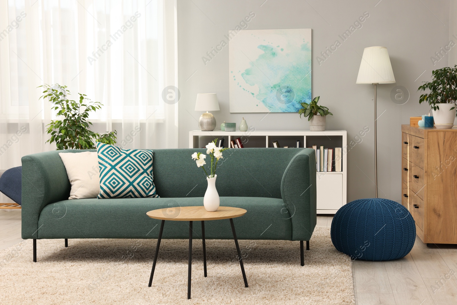 Photo of Soft sofa, coffee table, pouf, houseplants and chest of drawers near grey wall in living room. Interior design