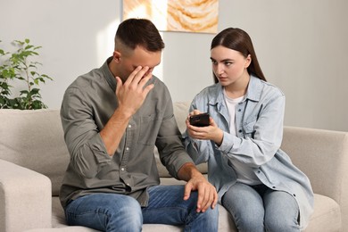 Wife showing smartphone with proofs to her unfaithful husband at home