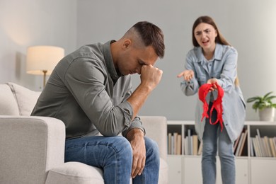 Emotional wife with mistress bra as proof screaming at her unfaithful husband while he ignoring her indoors, selective focus