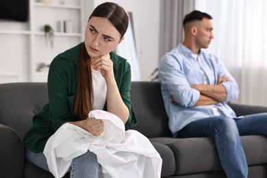 Frustrated wife holding shirt with lipstick marks as proof of her unfaithful husband at home