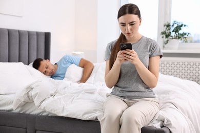 Photo of Jealous woman checking husband's smartphone while he sleeping in bedroom, selective focus