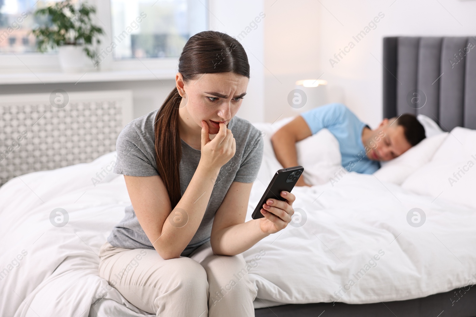 Photo of Nervous woman checking husband's smartphone while he sleeping in bedroom, selective focus