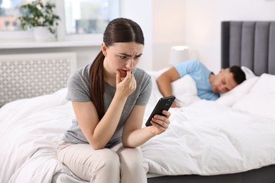 Photo of Nervous woman checking husband's smartphone while he sleeping in bedroom, selective focus