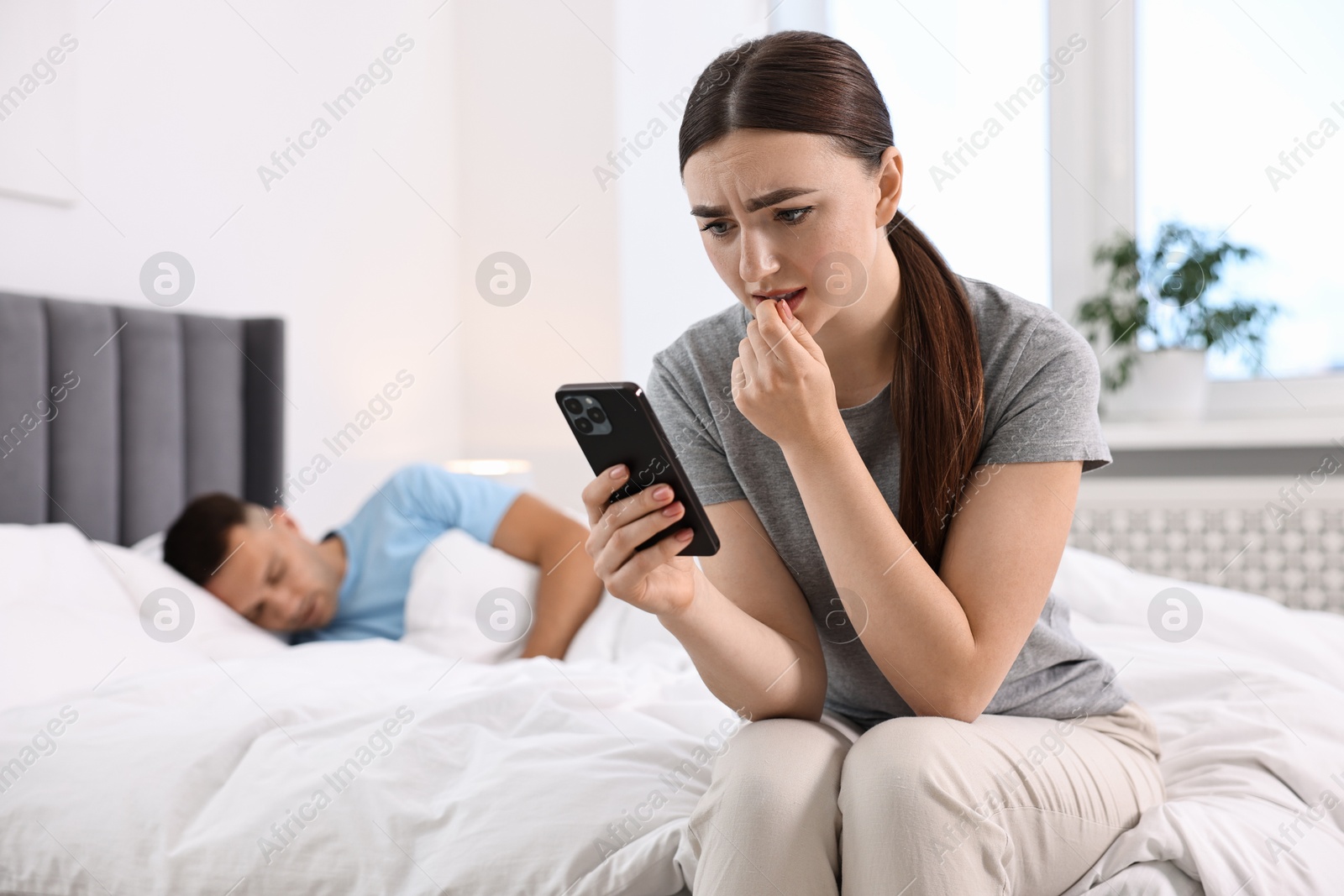 Photo of Nervous woman checking husband's smartphone while he sleeping in bedroom, selective focus