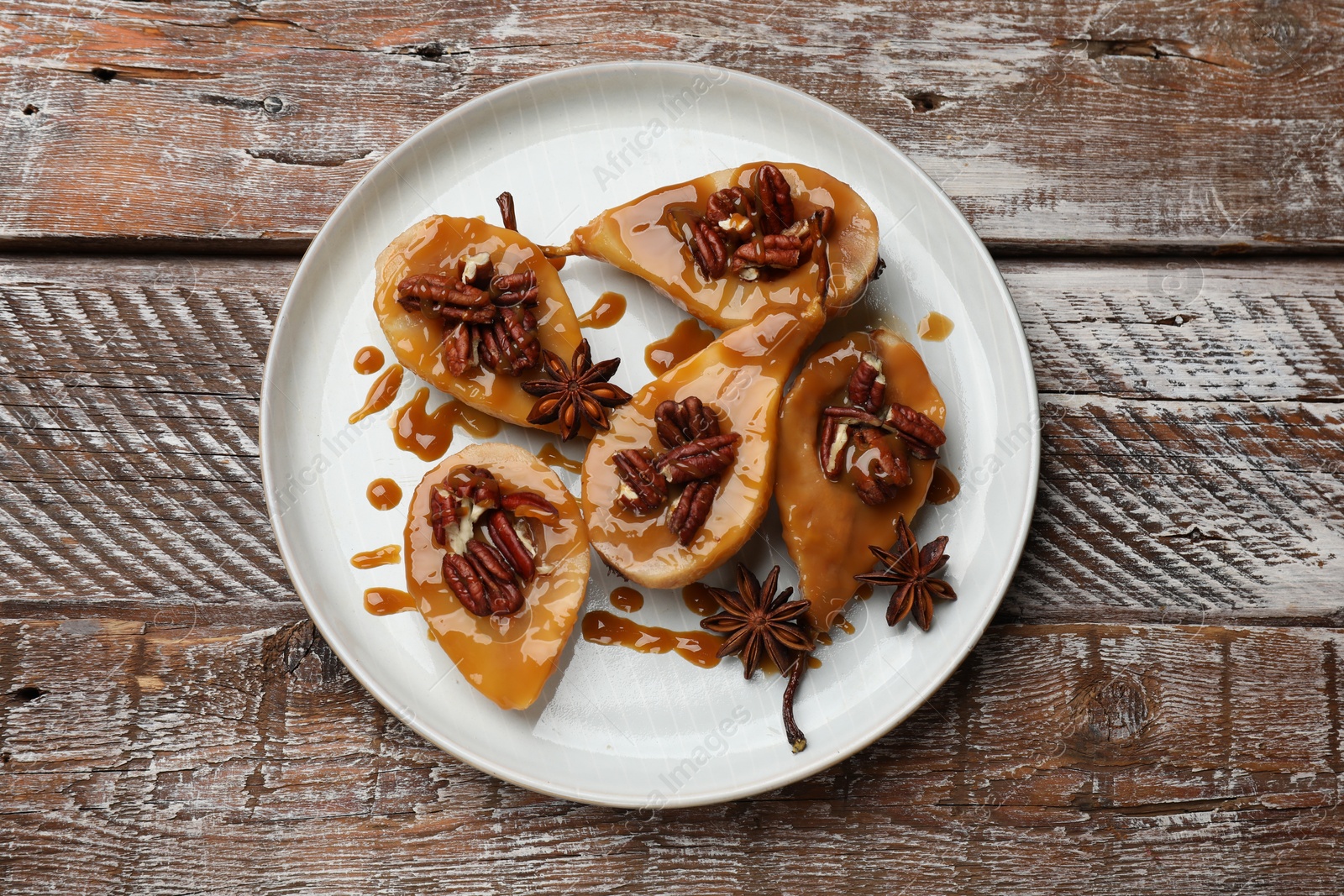 Photo of Delicious pears with caramel sauce, pecan nuts and anise stars on wooden table, top view