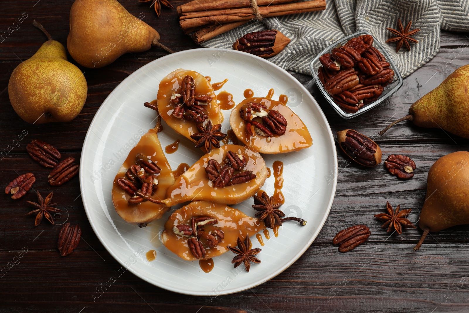 Photo of Delicious pears with caramel sauce, pecan nuts and spices on wooden table, flat lay