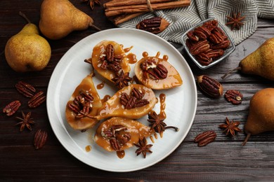 Photo of Delicious pears with caramel sauce, pecan nuts and spices on wooden table, flat lay