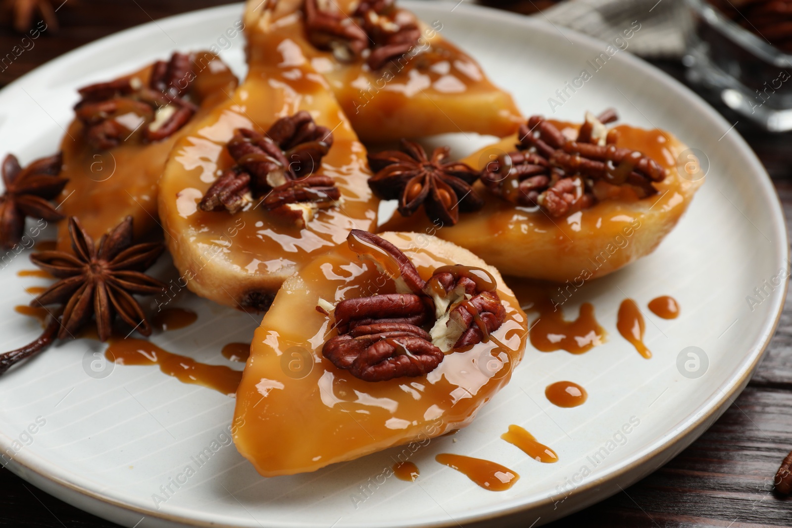 Photo of Delicious pears with caramel sauce, pecan nuts and anise stars on table, closeup