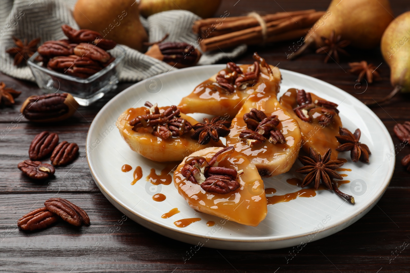 Photo of Delicious pears with caramel sauce, pecan nuts and anise stars on wooden table, closeup