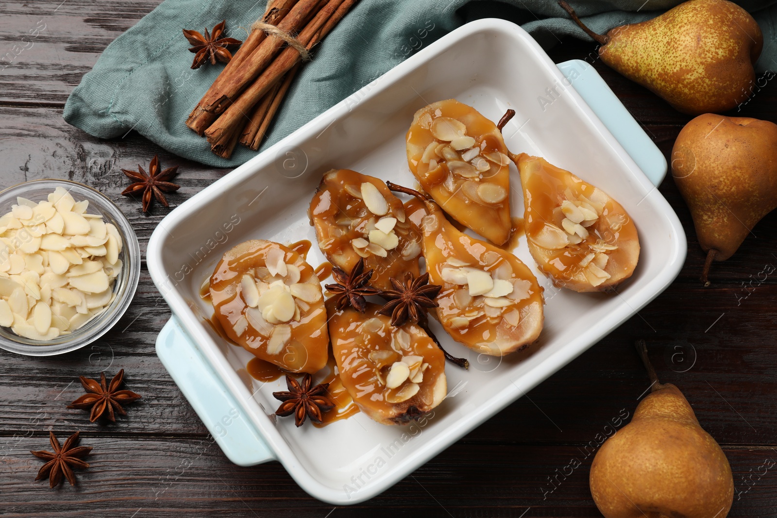 Photo of Delicious pears with caramel sauce, almond flakes and spices on wooden table, top view