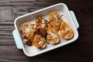 Photo of Delicious pears with caramel sauce, almond flakes and anise stars in baking dish on wooden table, top view