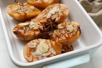 Photo of Delicious pears with caramel sauce, almond flakes and anise stars in baking dish on table, closeup