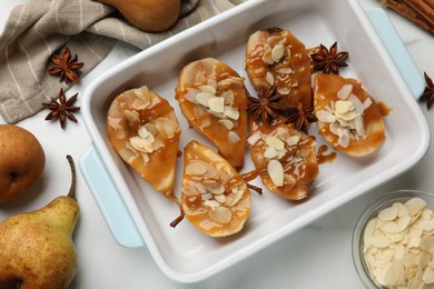 Photo of Delicious pears with caramel sauce, almond flakes and spices on white marble table, flat lay