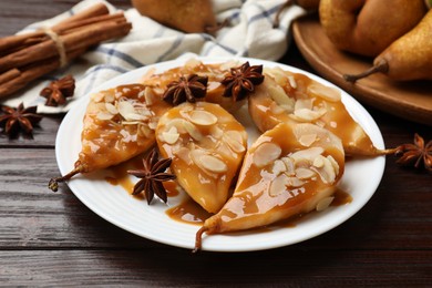 Photo of Delicious pears with caramel sauce, almond flakes and spices on wooden table, closeup