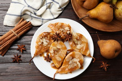 Photo of Delicious pears with caramel sauce, almond flakes and spices on wooden table, top view