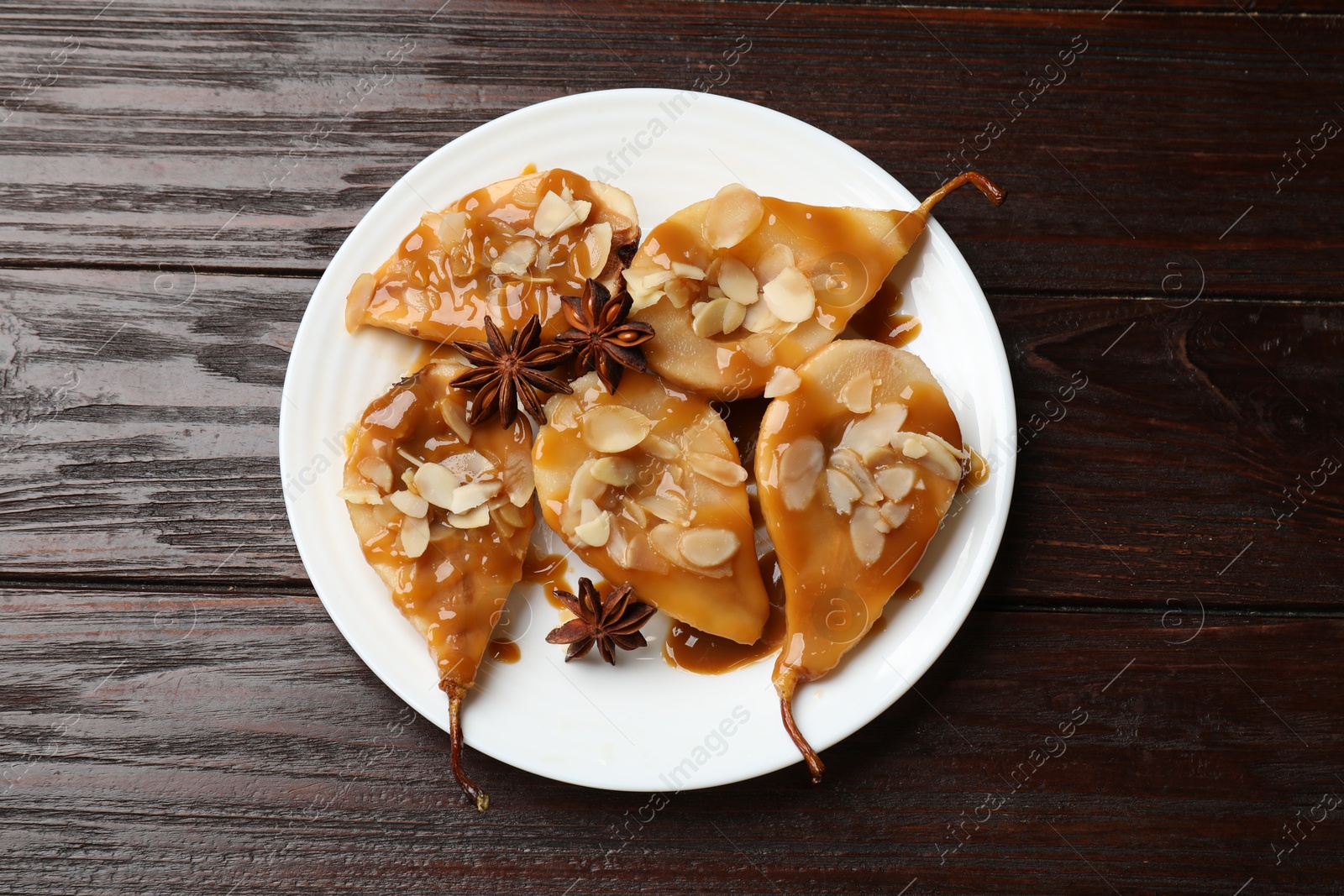 Photo of Delicious pears with caramel sauce, almond flakes and anise stars on wooden table, top view