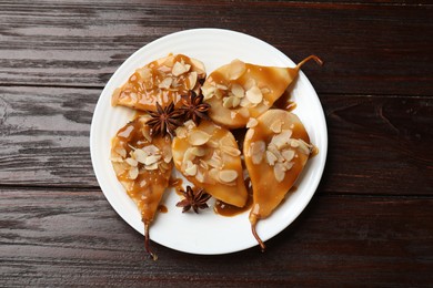 Photo of Delicious pears with caramel sauce, almond flakes and anise stars on wooden table, top view