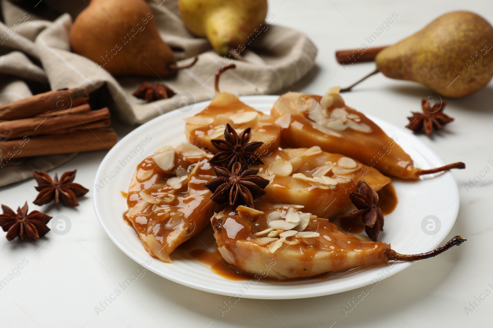 Photo of Delicious pears with caramel sauce, almond flakes and anise stars on white table, closeup