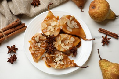 Photo of Delicious pears with caramel sauce, almond flakes and spices on white marble table, flat lay