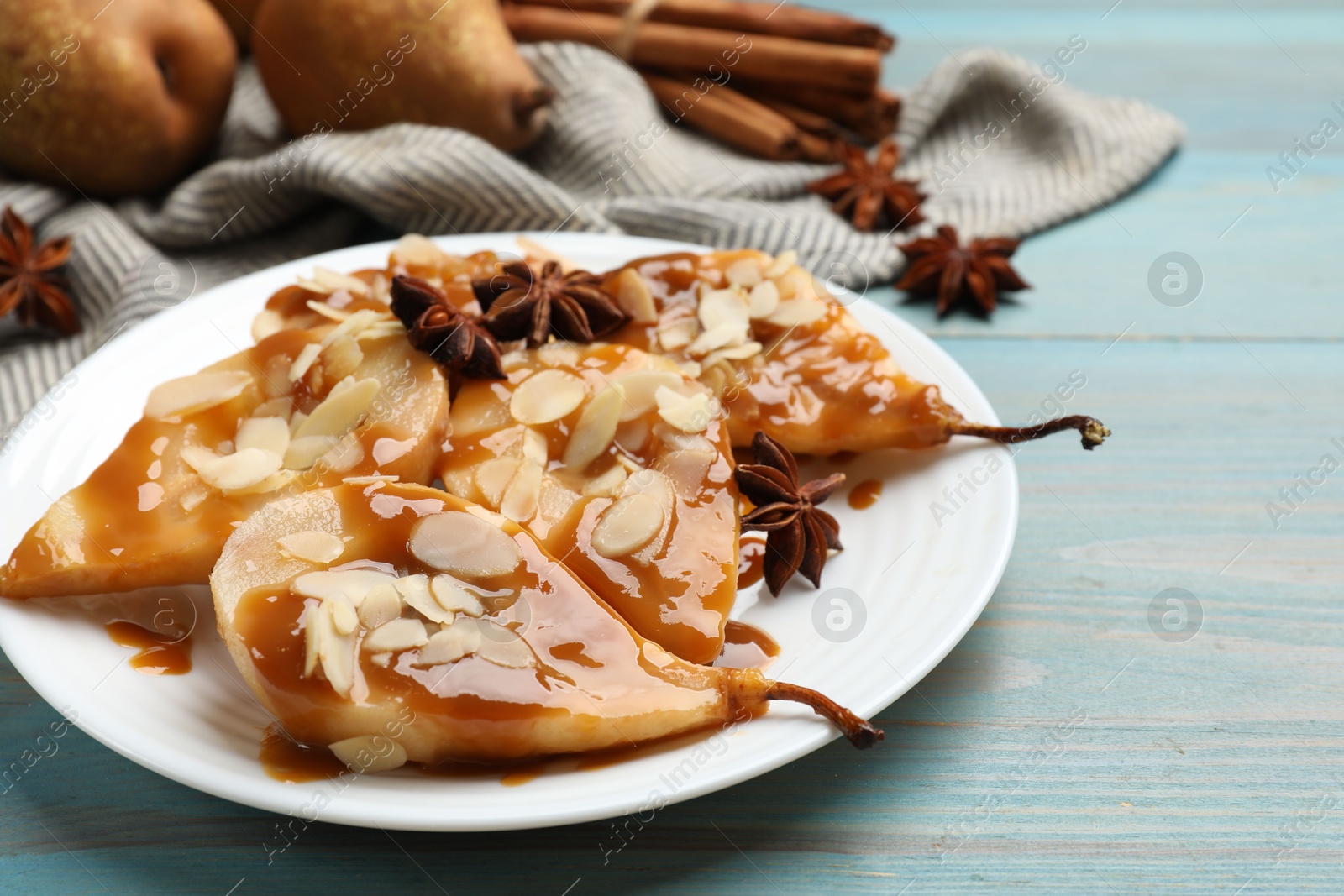 Photo of Delicious pears with caramel sauce, almond flakes and anise stars on light blue wooden table, closeup