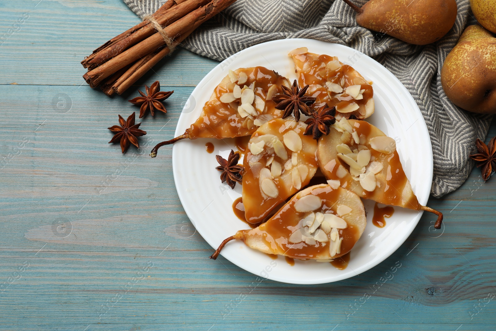 Photo of Delicious pears with caramel sauce, almond flakes and spices on light blue wooden table, flat lay