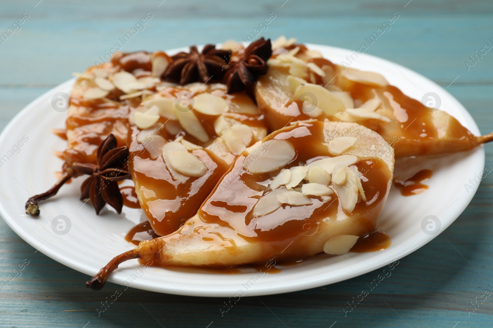 Photo of Delicious pears with caramel sauce, almond flakes and anise stars on light blue wooden table, closeup