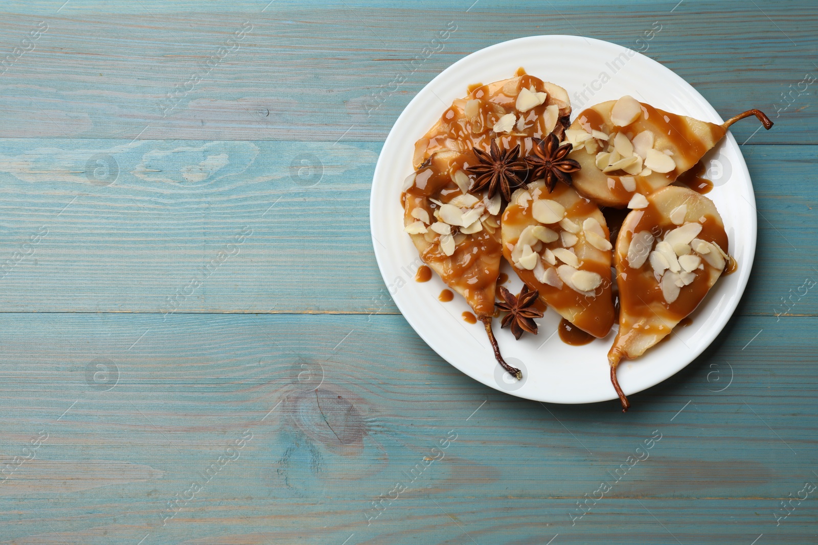 Photo of Delicious pears with caramel sauce, almond flakes and anise stars on light blue wooden table, top view. Space for text