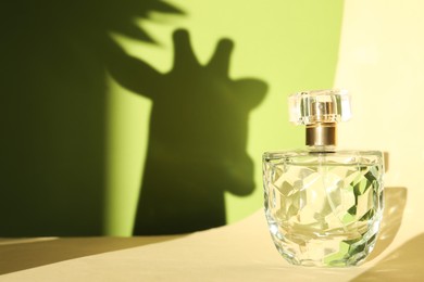 Photo of Beautiful perfume bottle on color background against shadow in shape of giraffe