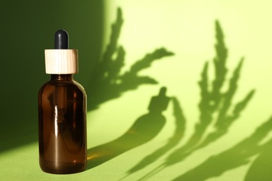 Photo of Bottle of skin care product on light green background with beautiful shadows