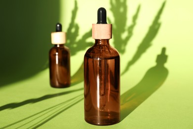 Photo of Bottles of skin care product on light green background with beautiful shadows