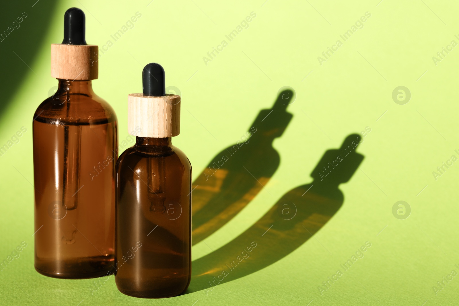 Photo of Bottles of skin care product casting shadows on light green background