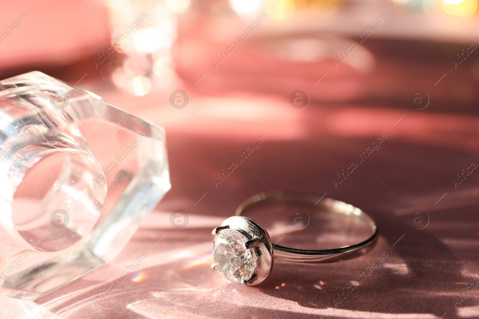 Photo of Beautiful ring and bottle of perfume on light pink background, closeup