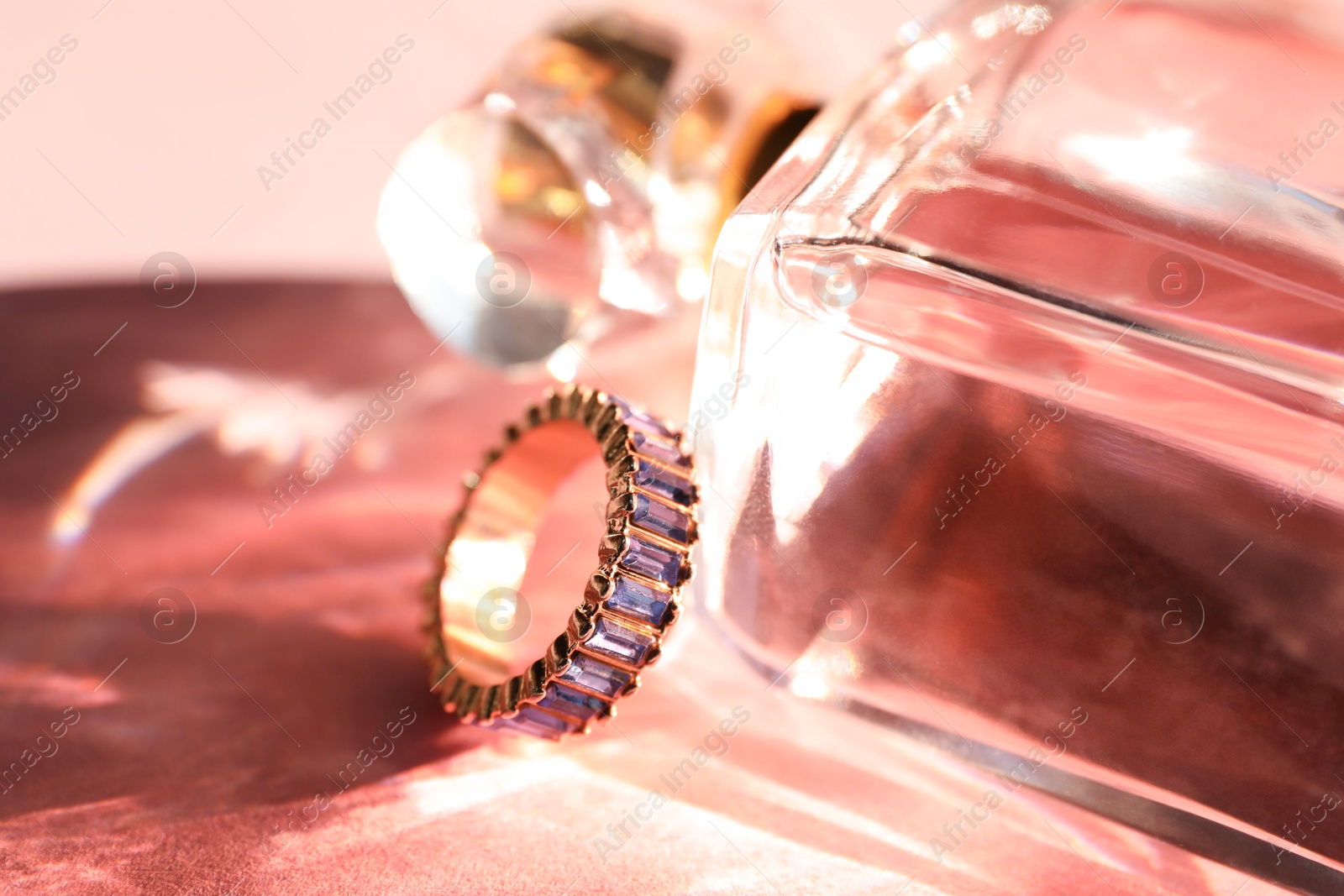 Photo of Beautiful ring and bottle of perfume on light pink background, closeup