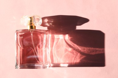 Photo of Beautiful perfume bottle casting shadow on light pink background, top view