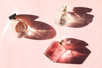 Photo of Beautiful perfume bottles casting shadows on light pink background, flat lay