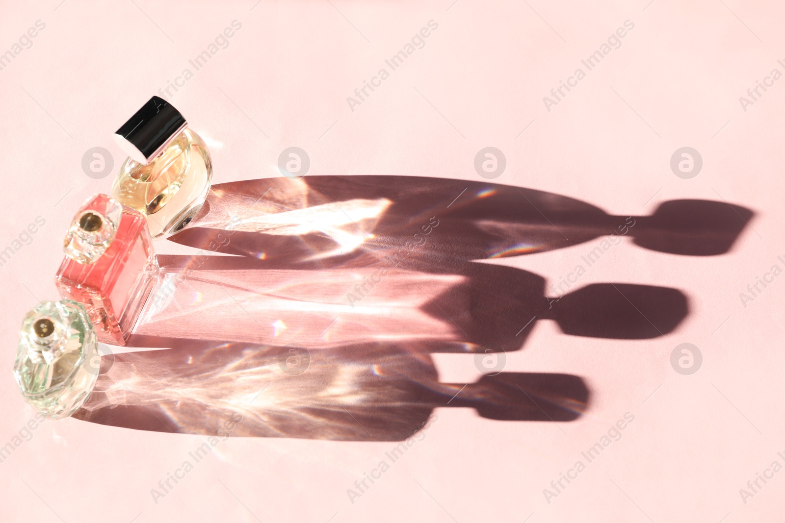 Photo of Beautiful perfume bottles casting shadows on light pink background, above view