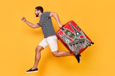 Happy traveler with suitcase covered in stickers of famous landmarks running on orange background