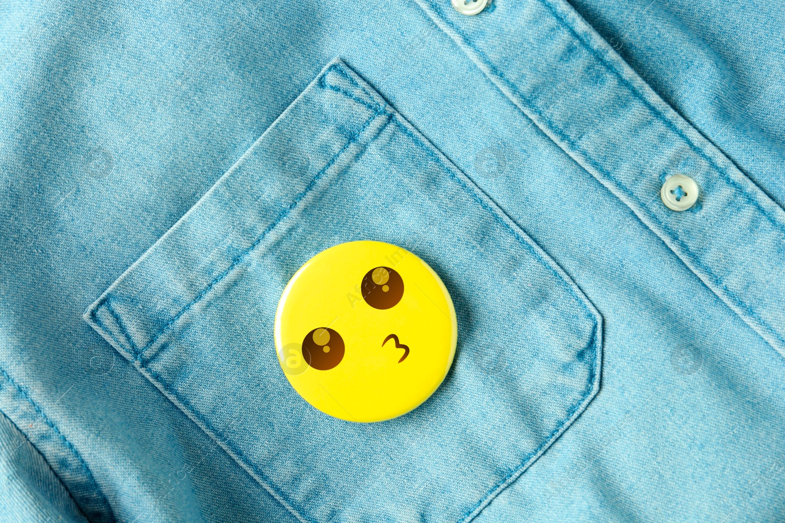 Image of Badge with kissing face attached to pocket of denim shirt