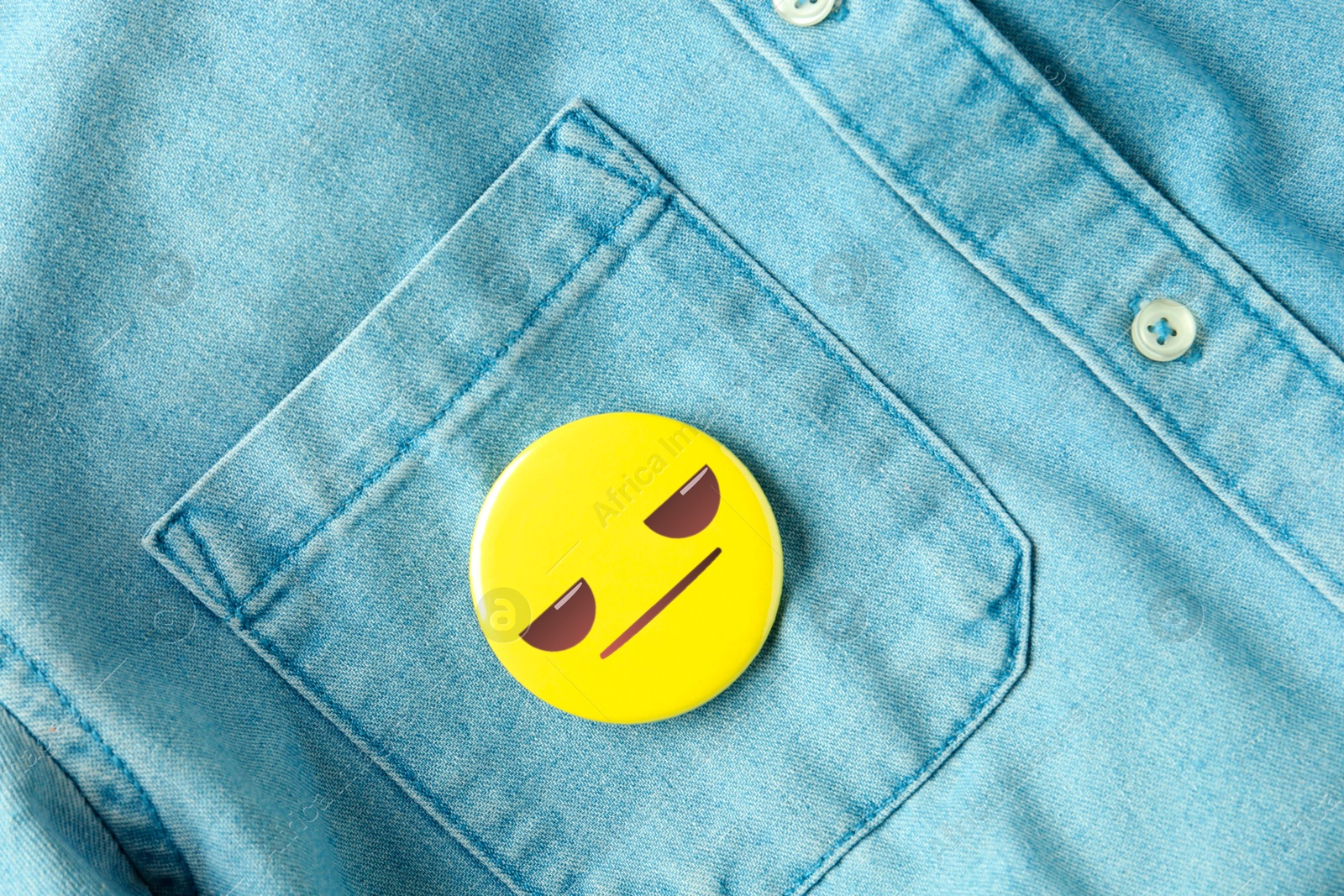 Image of Badge with distrustful or displeased face attached to pocket of denim shirt