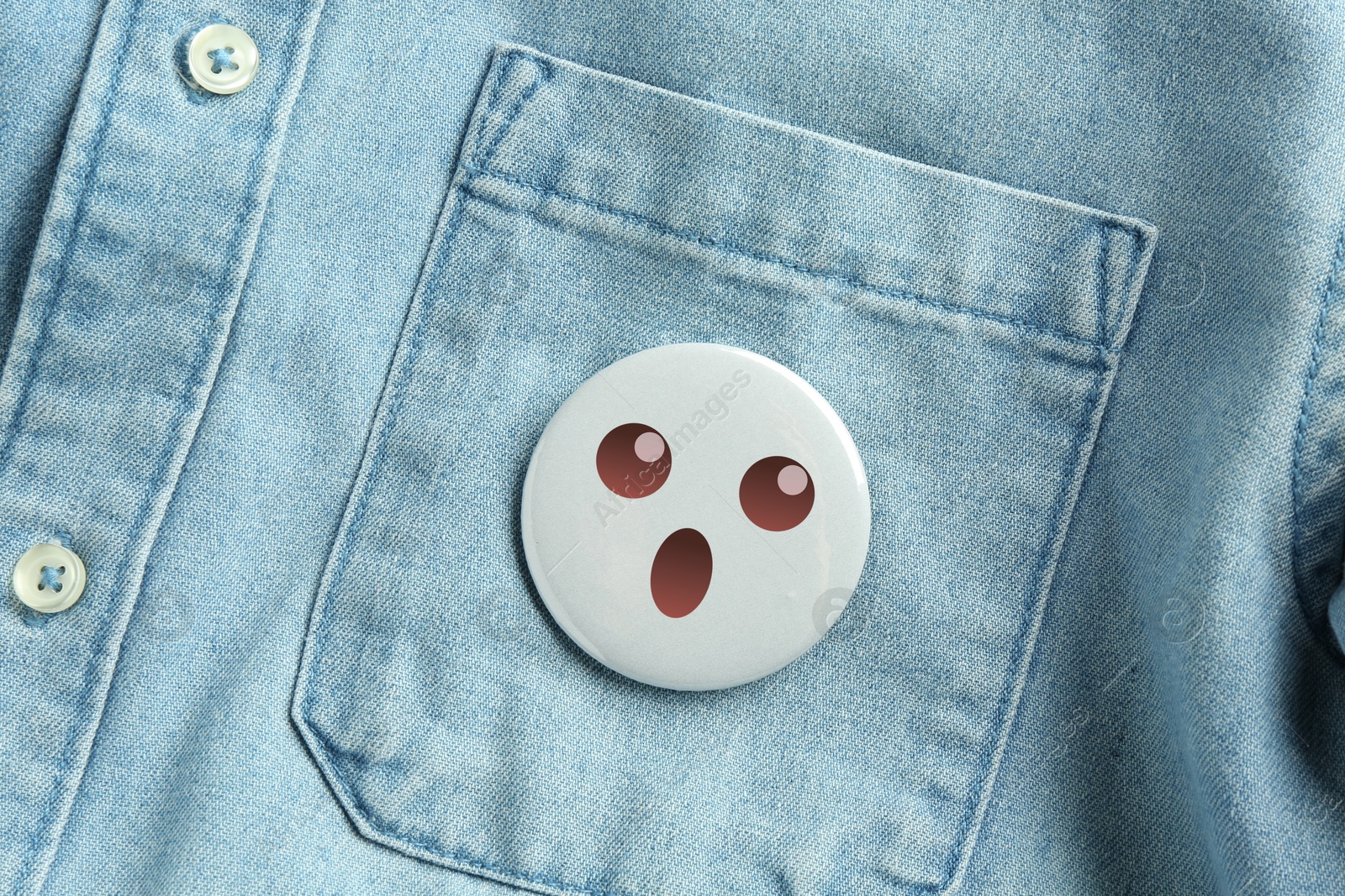 Image of Badge with shocked or surprised face attached to pocket of denim shirt