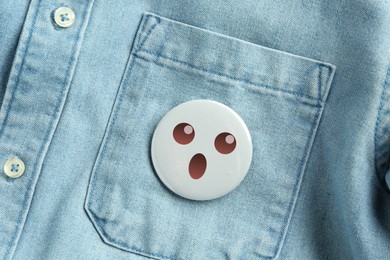 Image of Badge with shocked or surprised face attached to pocket of denim shirt