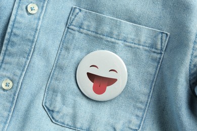 Image of Badge with face showing tongue attached to pocket of denim shirt