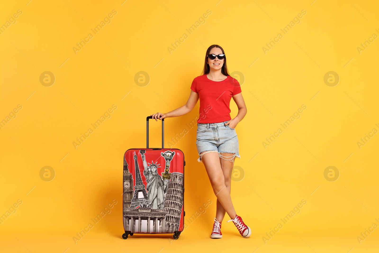 Image of Happy traveler with suitcase covered in stickers of famous landmarks on orange background