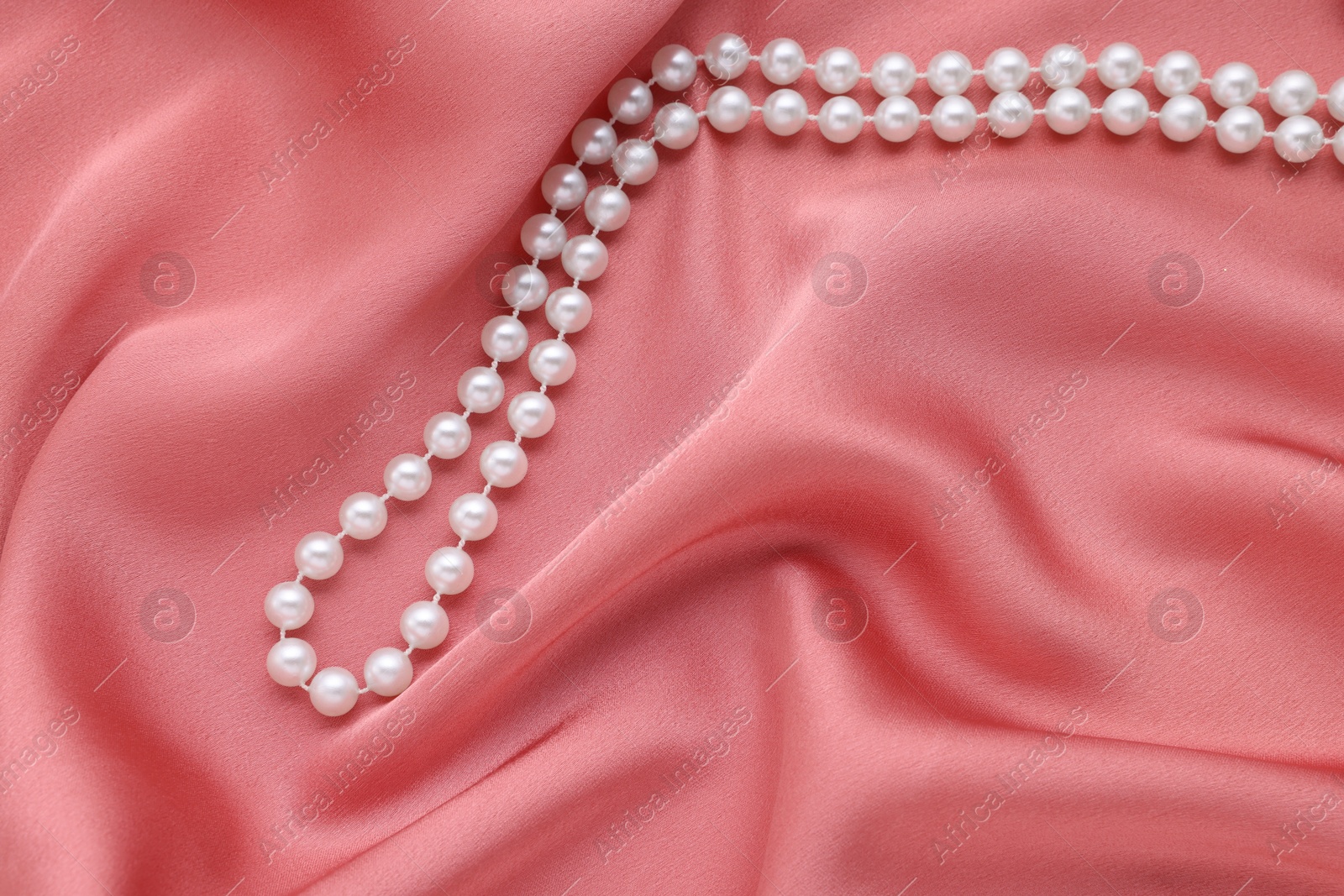 Photo of Elegant pearl necklace on pink fabric, top view